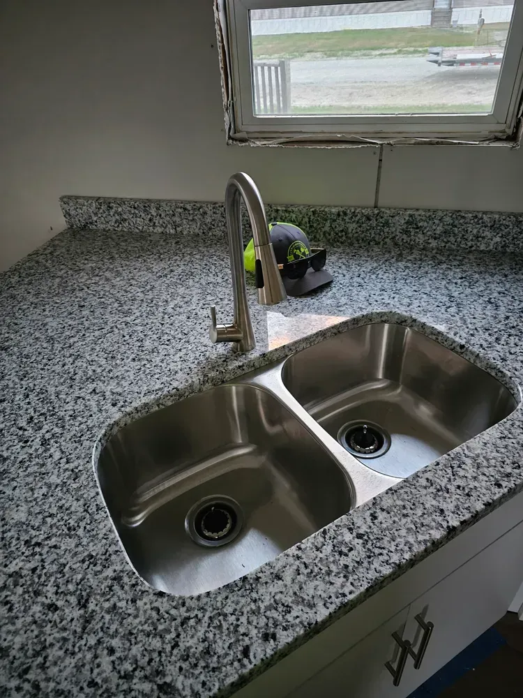 A kitchen sink with two sinks and a faucet on a granite counter top.