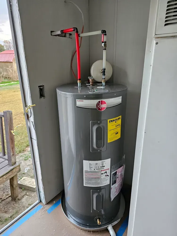 A gray water heater is sitting in a room next to a door.
