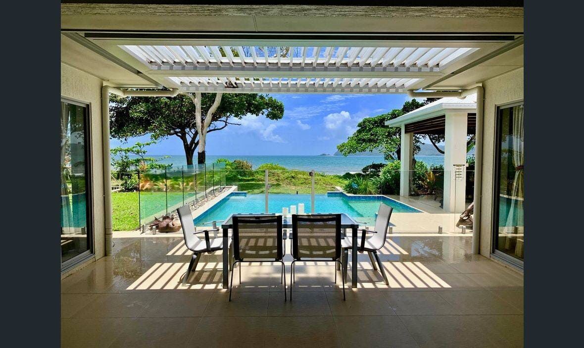 A Patio With a Table and Chairs Overlooking a Swimming Pool and the Ocean — Coral Coast Building & Management in Cannon Valley, QLD