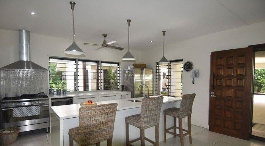 A Kitchen With a Stove , Sink , Chairs and a Ceiling Fan — Coral Coast Building & Management in Cannon Valley, QLD