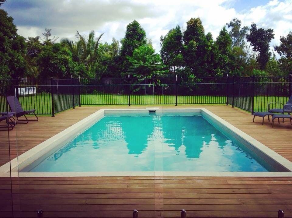 A Large Swimming Pool With a Wooden Deck and Chairs Around It — Coral Coast Building & Management in Cannon Valley, QLD