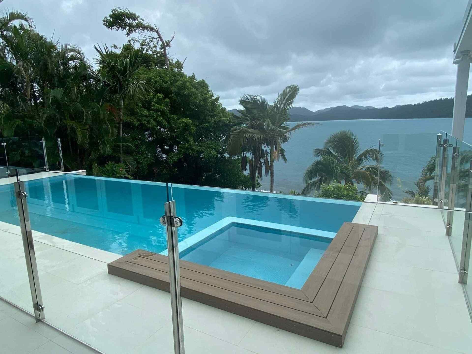A Large Swimming Pool With a Hot Tub Next to It and a View of the Ocean — Coral Coast Building & Management in Cannon Valley, QLD