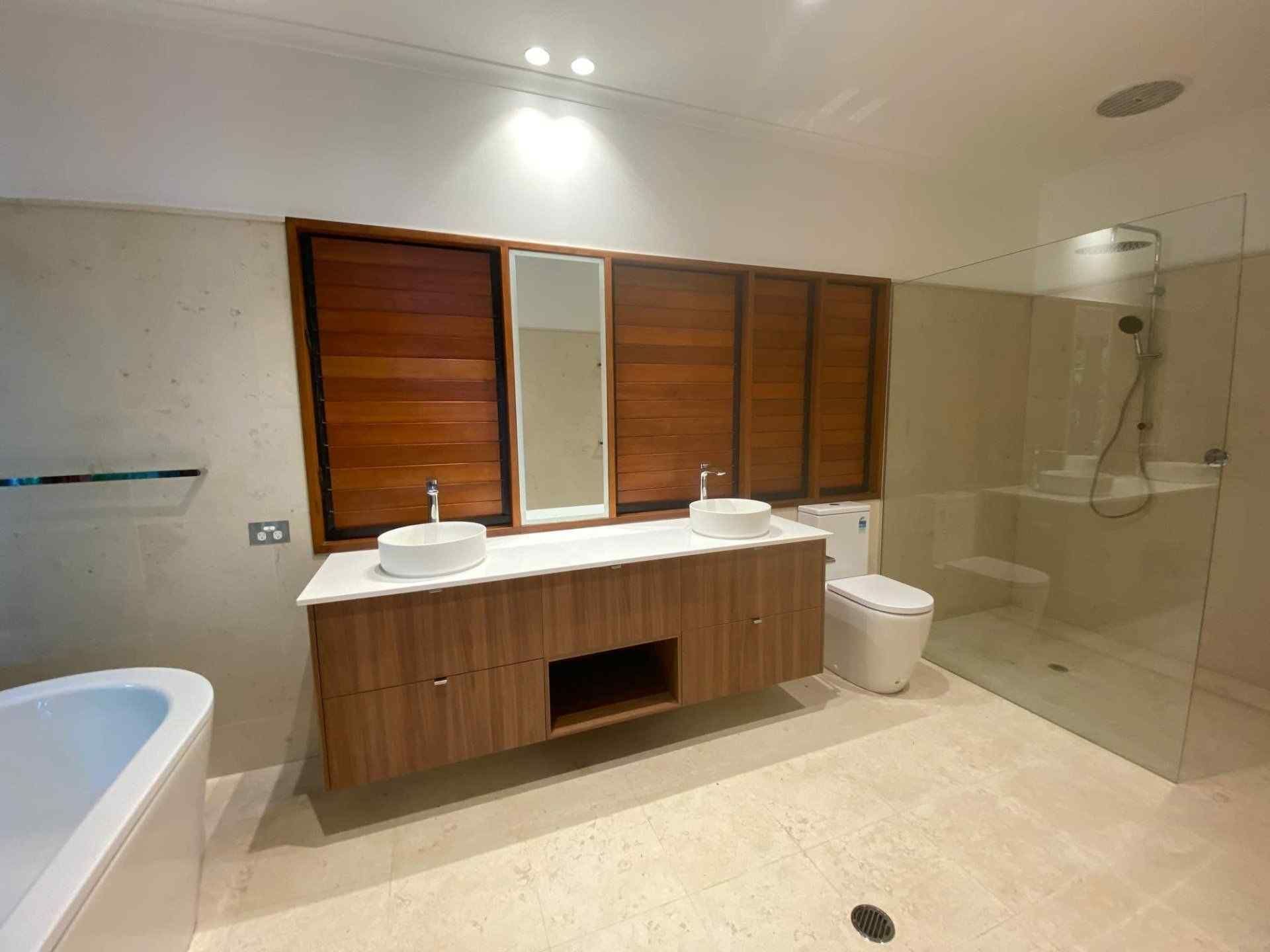 A Bathroom With Two Sinks , a Toilet , and a Walk in Shower — Coral Coast Building & Management in Cannon Valley, QLD