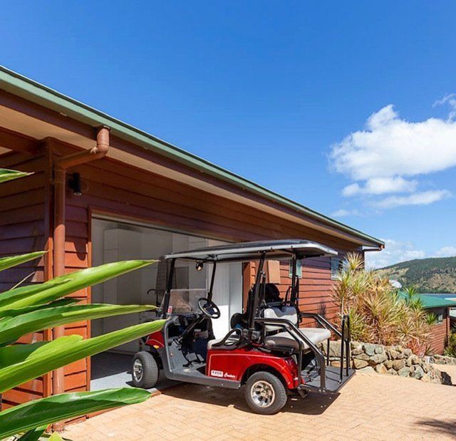 A Red Golf Cart is Parked in Front of a House — Coral Coast Building & Management in Cannon Valley, QLD