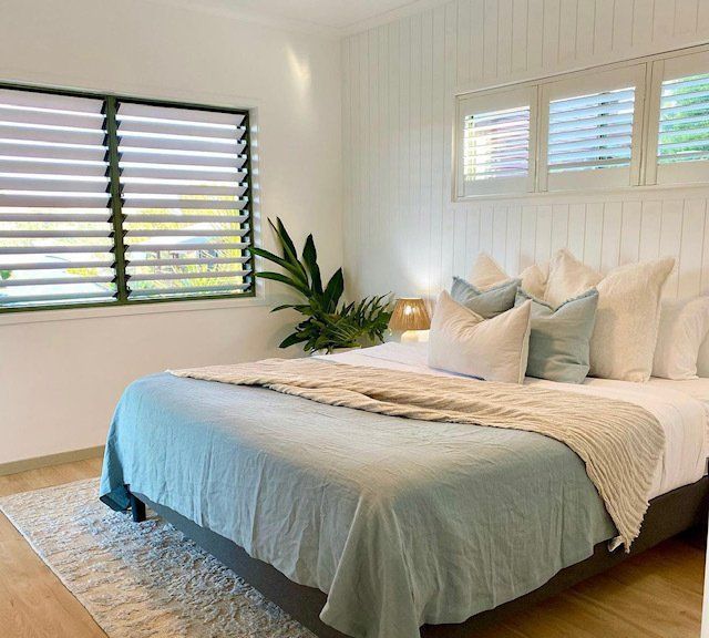 A Bedroom With a Bed , Pillows , and Shutters on the Windows — Coral Coast Building & Management in Cannon Valley, QLD