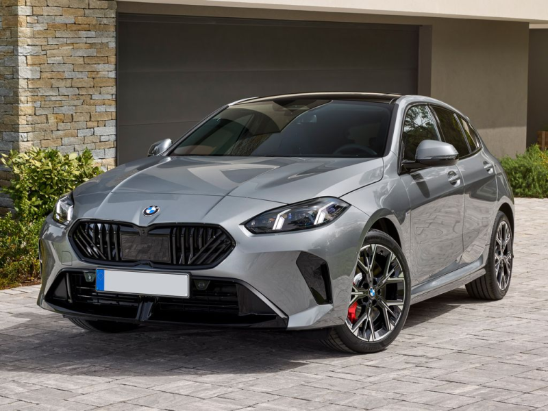 Un'auto compatta BMW color argento parcheggiata davanti a una casa moderna con porta da garage.