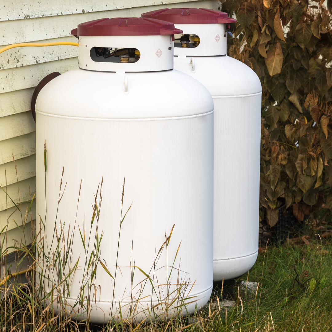 two white propane tanks with red lids on the side of a house