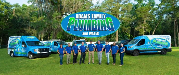 A group of people standing in front of a sign that says adam's family plumbing and water