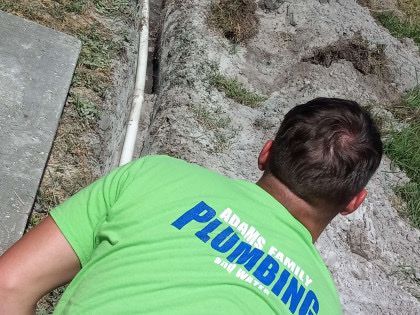 A man wearing a green adams family plumbing shirt