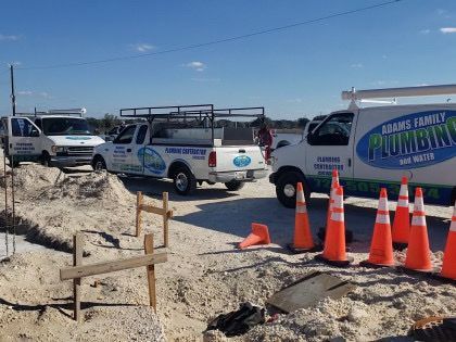 A row of plumbing trucks are parked on a dirt road