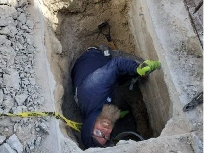 A man is laying in a hole with a shovel.