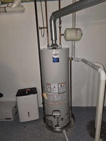 A water heater is sitting in a basement next to a humidifier.