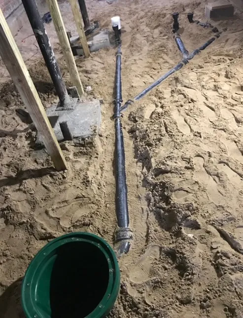 A green bucket is sitting in the dirt next to a pipe.