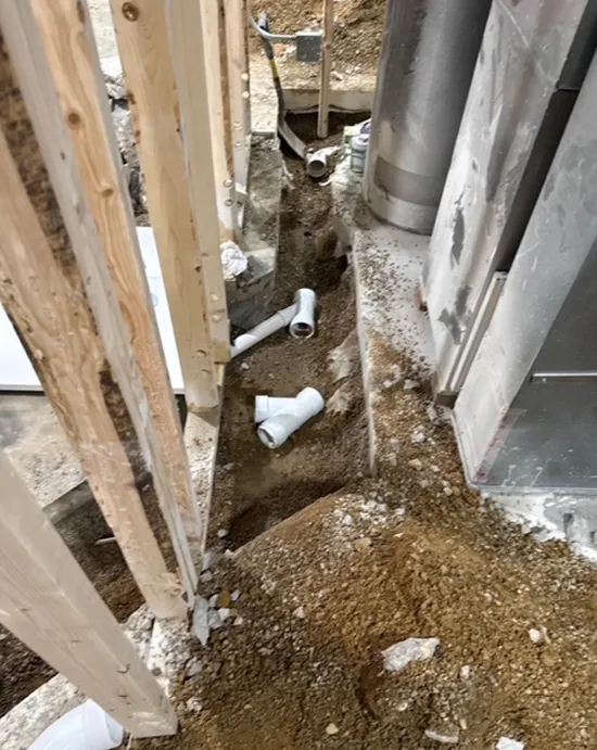 A bunch of pipes are laying in the dirt next to a wall.