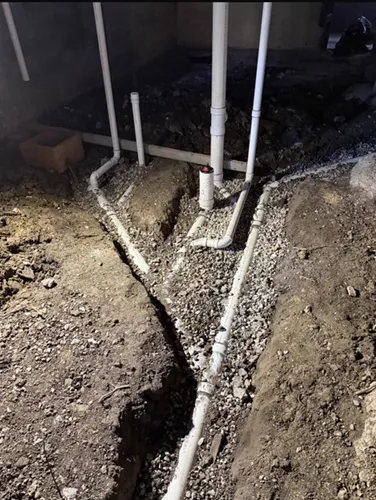 A bunch of pipes are laying in the dirt in a basement.