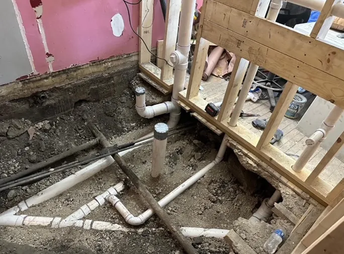 A bunch of pipes are laying on the ground in a room under construction.