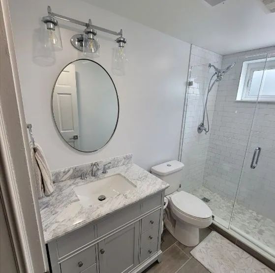 A bathroom with a sink , toilet , shower and mirror.