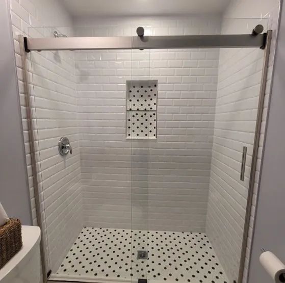 A bathroom with white tiles and a sliding glass shower door.