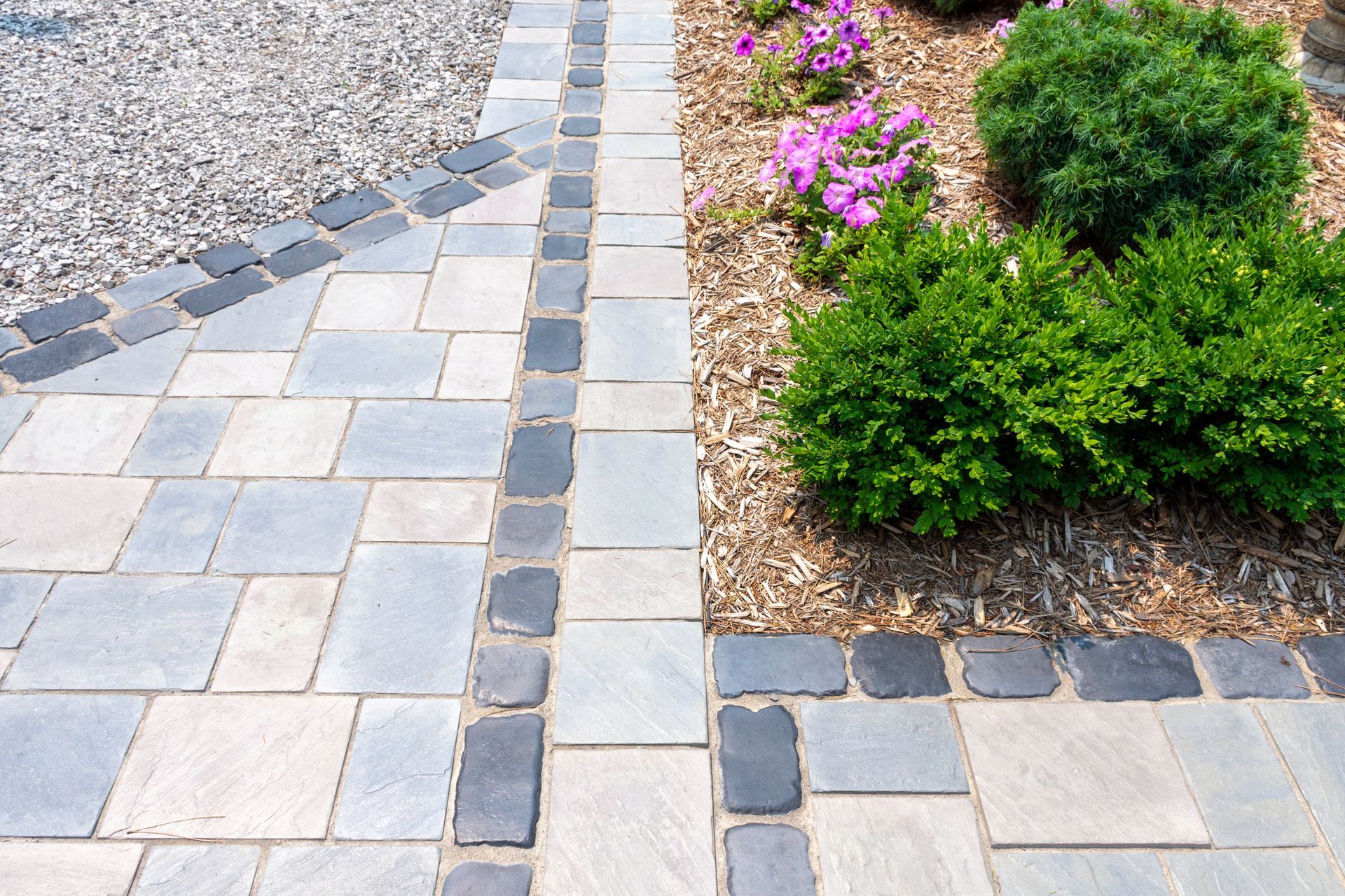 A brick walkway leading to a garden with flowers and bushes.
