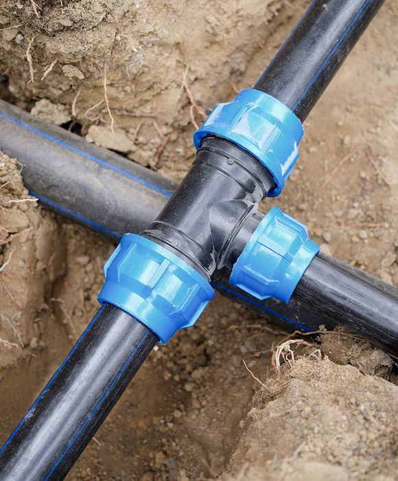 Black plastic pipes connected with blue fittings in a trench, likely for irrigation.