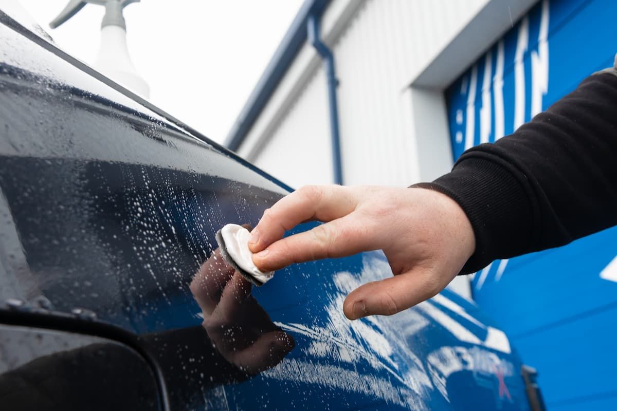 A man is polishing a red car in front of an american flag