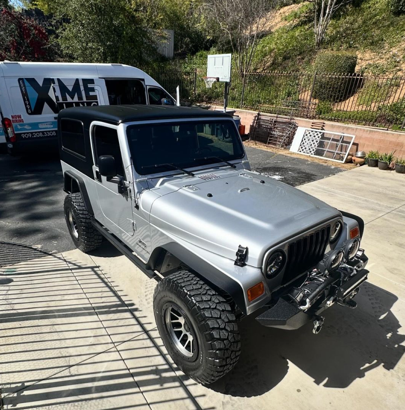 A silver jeep is parked in front of a van that says xtreme