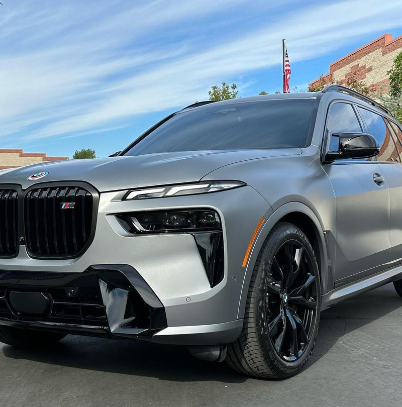 A silver bmw x7 is parked in front of a building