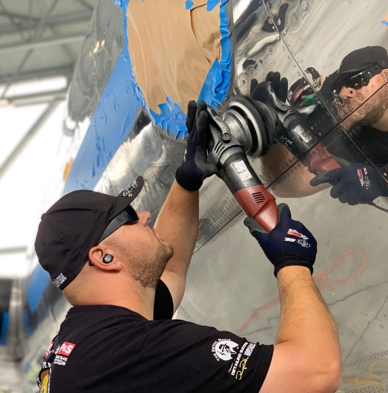 A man wearing a hat and sunglasses is polishing a plane