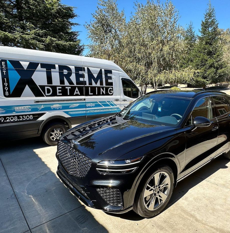 A black car is parked next to an xtreme detailing van