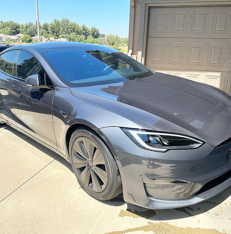 A gray tesla model s is parked in front of a garage door.