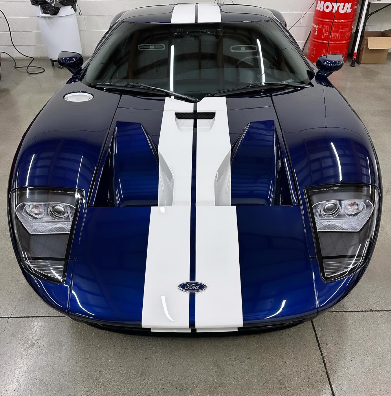 A blue sports car with white stripes is parked in front of a motul barrel