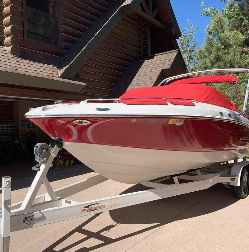 A red boat is on a trailer in front of a house