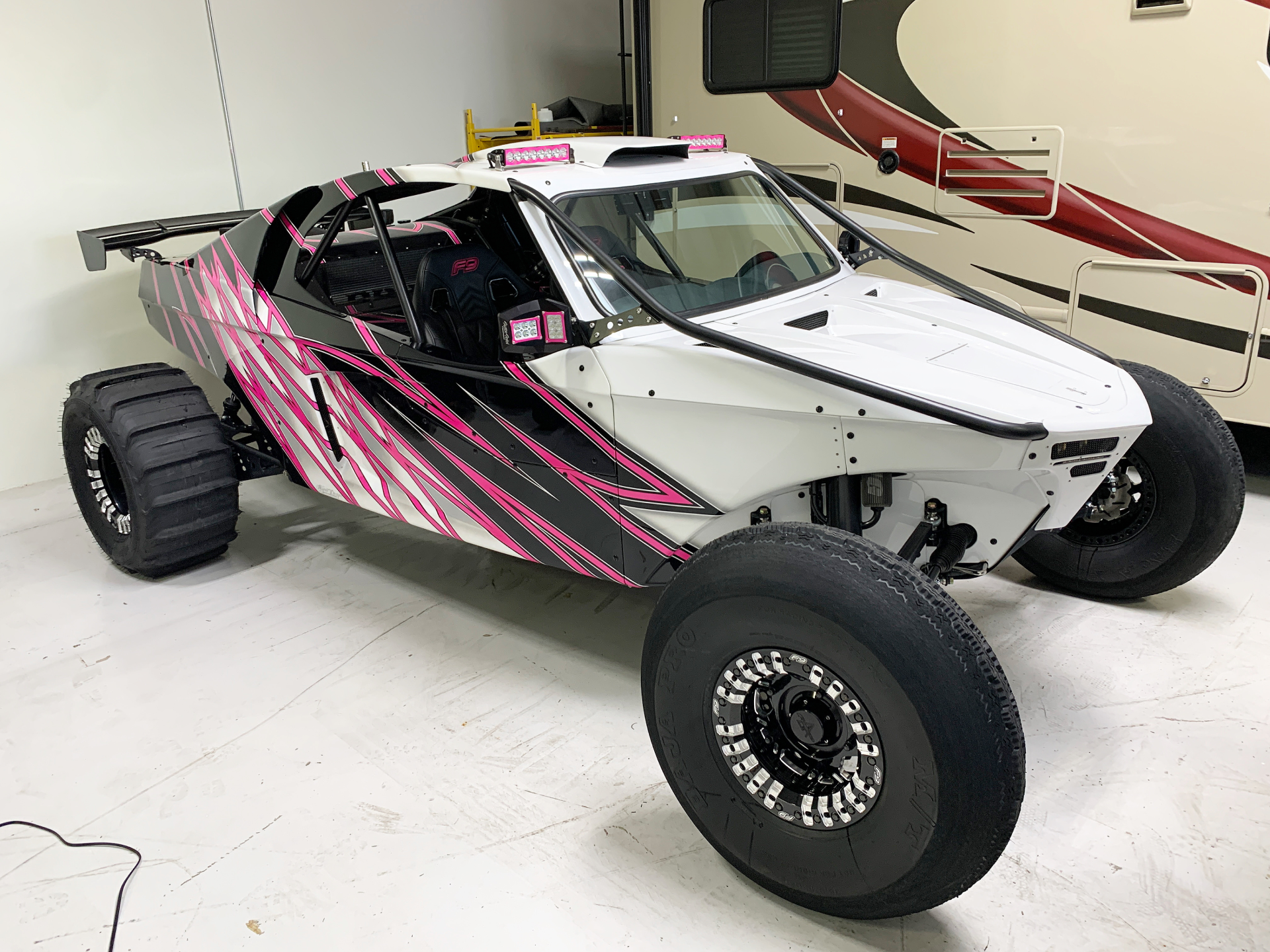 a white and pink buggy is parked in a garage next to a rv .