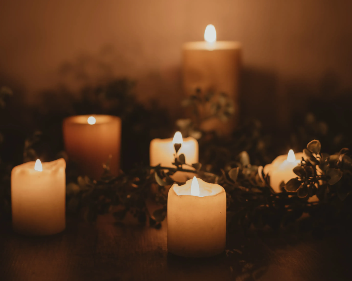 Five lit candles among greenery, warm lighting.