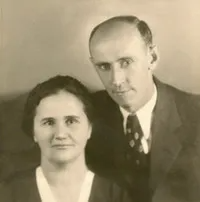 Older couple smiling, holding hands. Man in a suit, woman in blue.