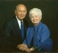 Older couple smiling, holding hands. Man in a suit, woman in blue.