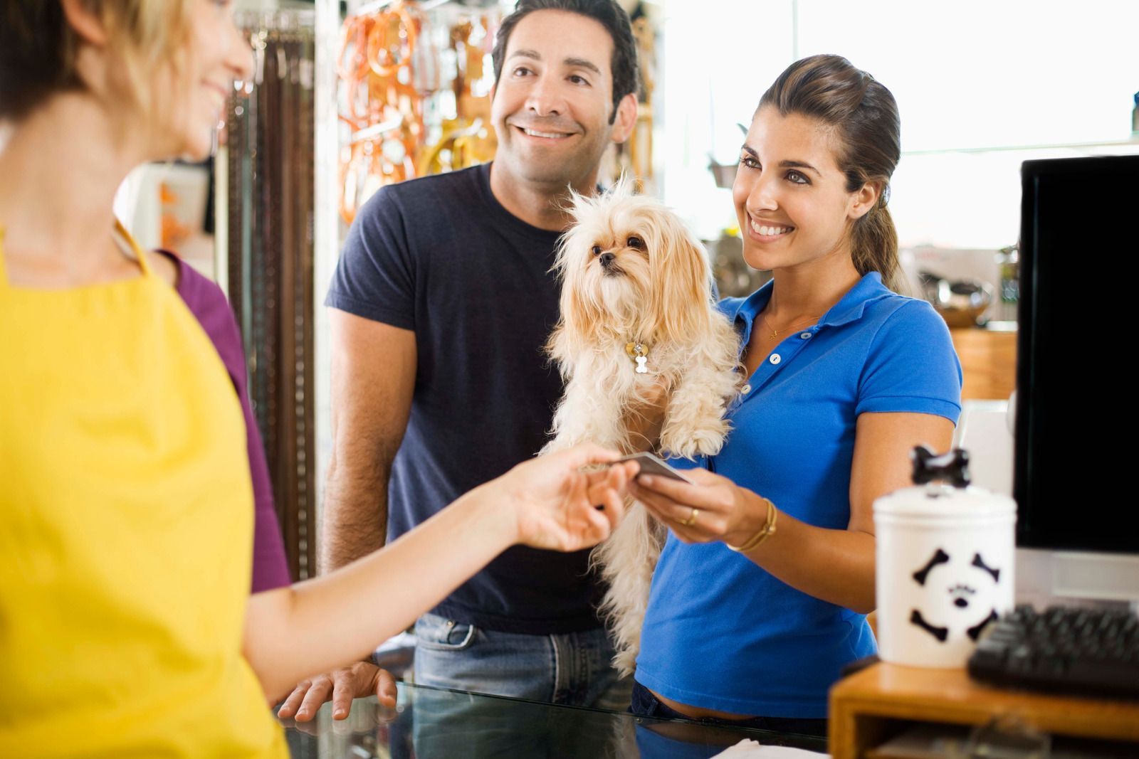 Couple buying pet supplies with their dog at a shop. The woman pays the cashier.
