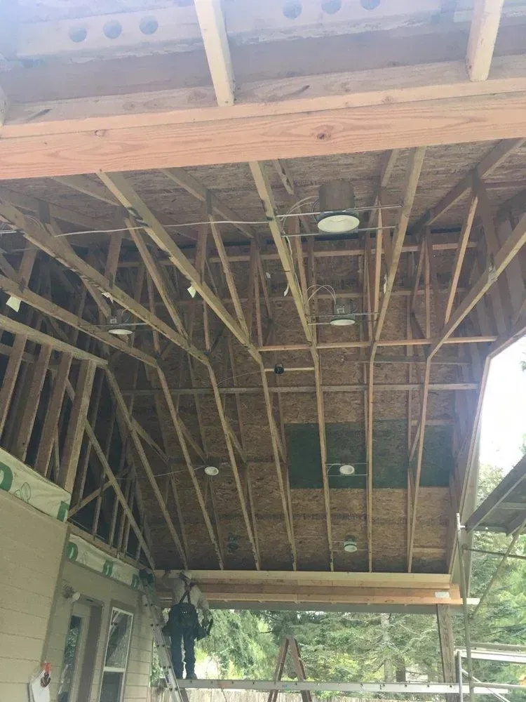 A man is standing on a ladder in the ceiling of a building under construction.