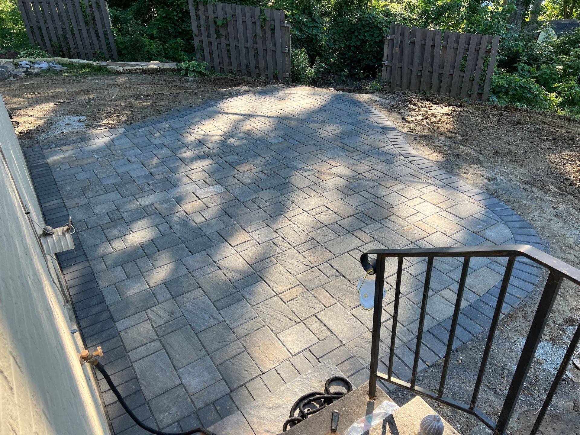 Paver patio with dark border, brown fencing, and metal railing.