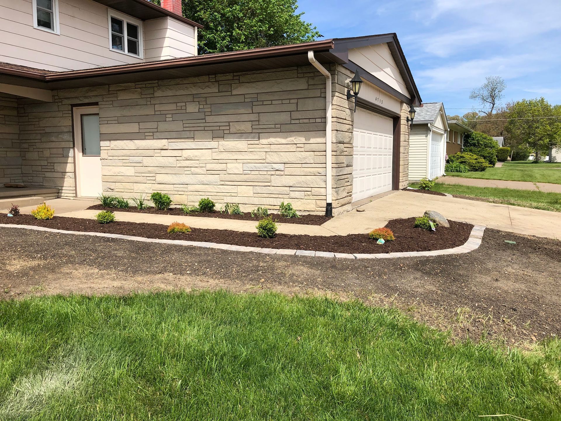 A house with a stone facade and a flower bed lining the driveway.