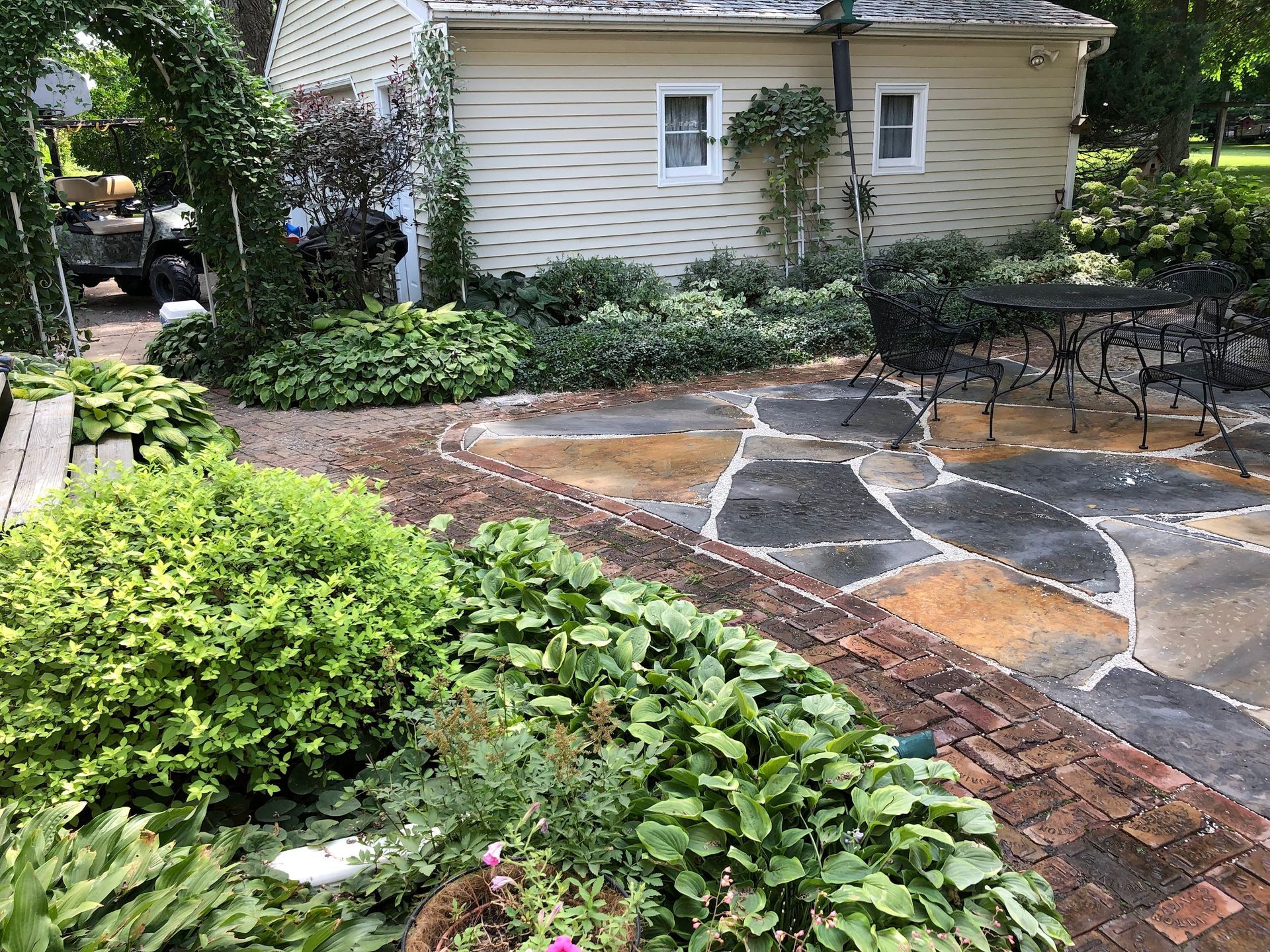 Stone patio with surrounding lush greenery and a beige garage in the background.