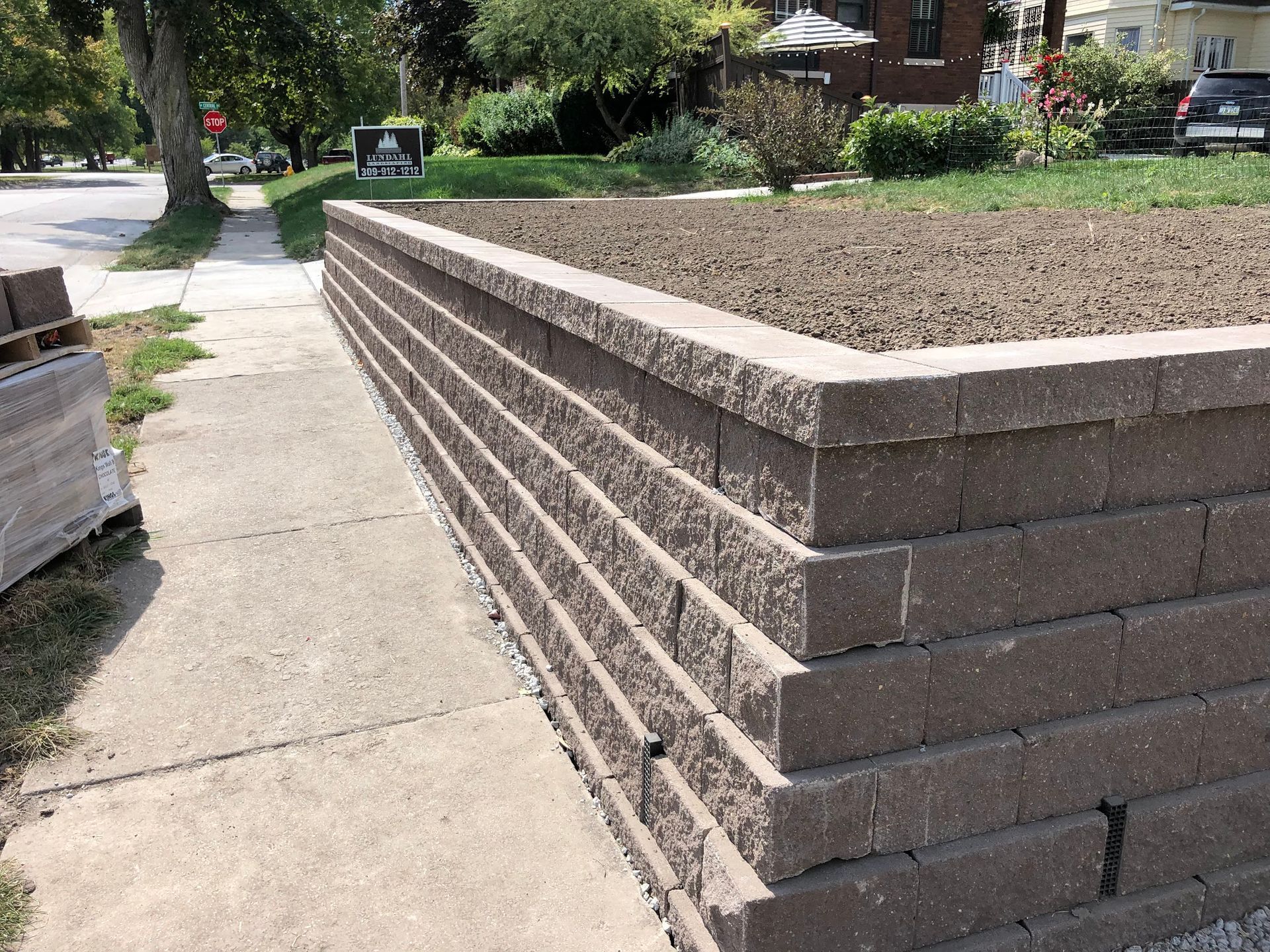 Retaining wall made of brown blocks next to a sidewalk, holding back dirt.