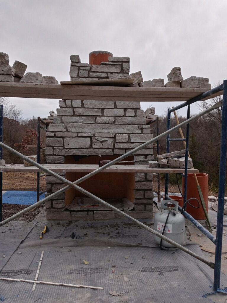 Stone chimney under construction, surrounded by scaffolding, on a cloudy day.