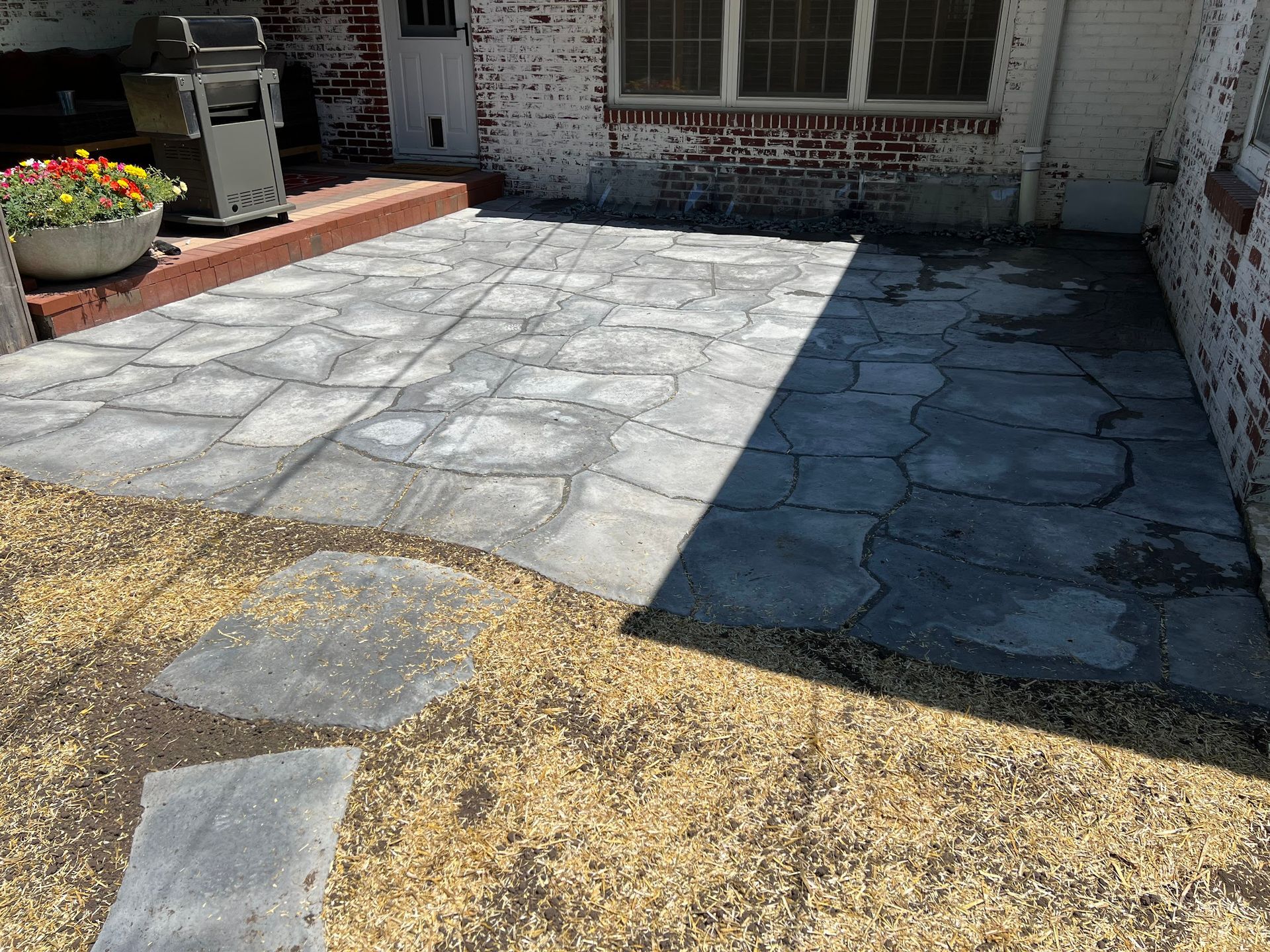 Concrete patio with cracks and a small rock border next to a brick building.