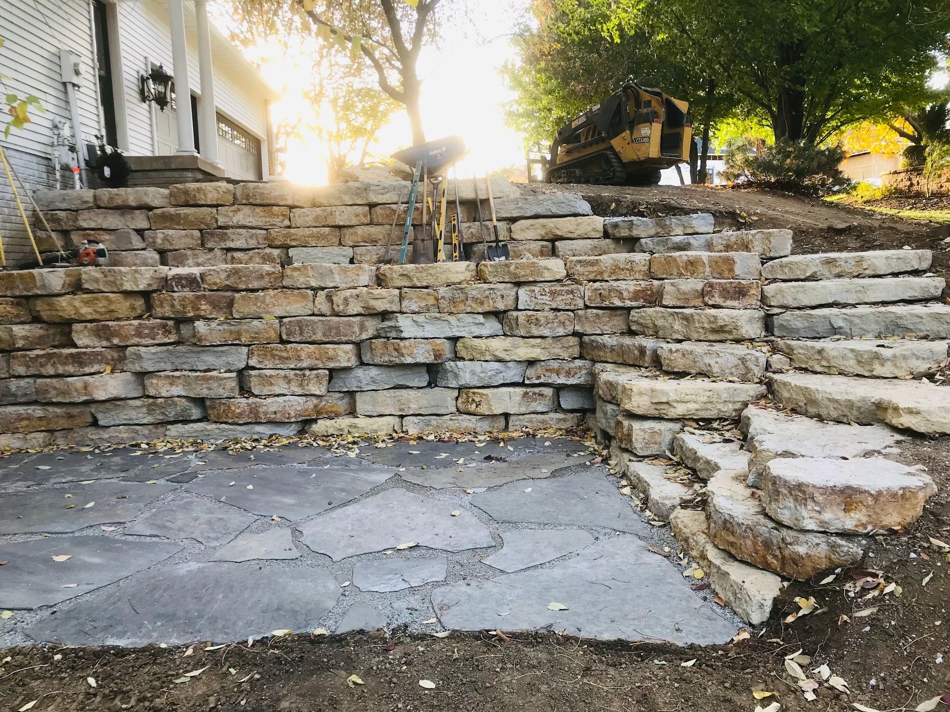 Stone steps and patio under construction, with a building and trees in the background.
