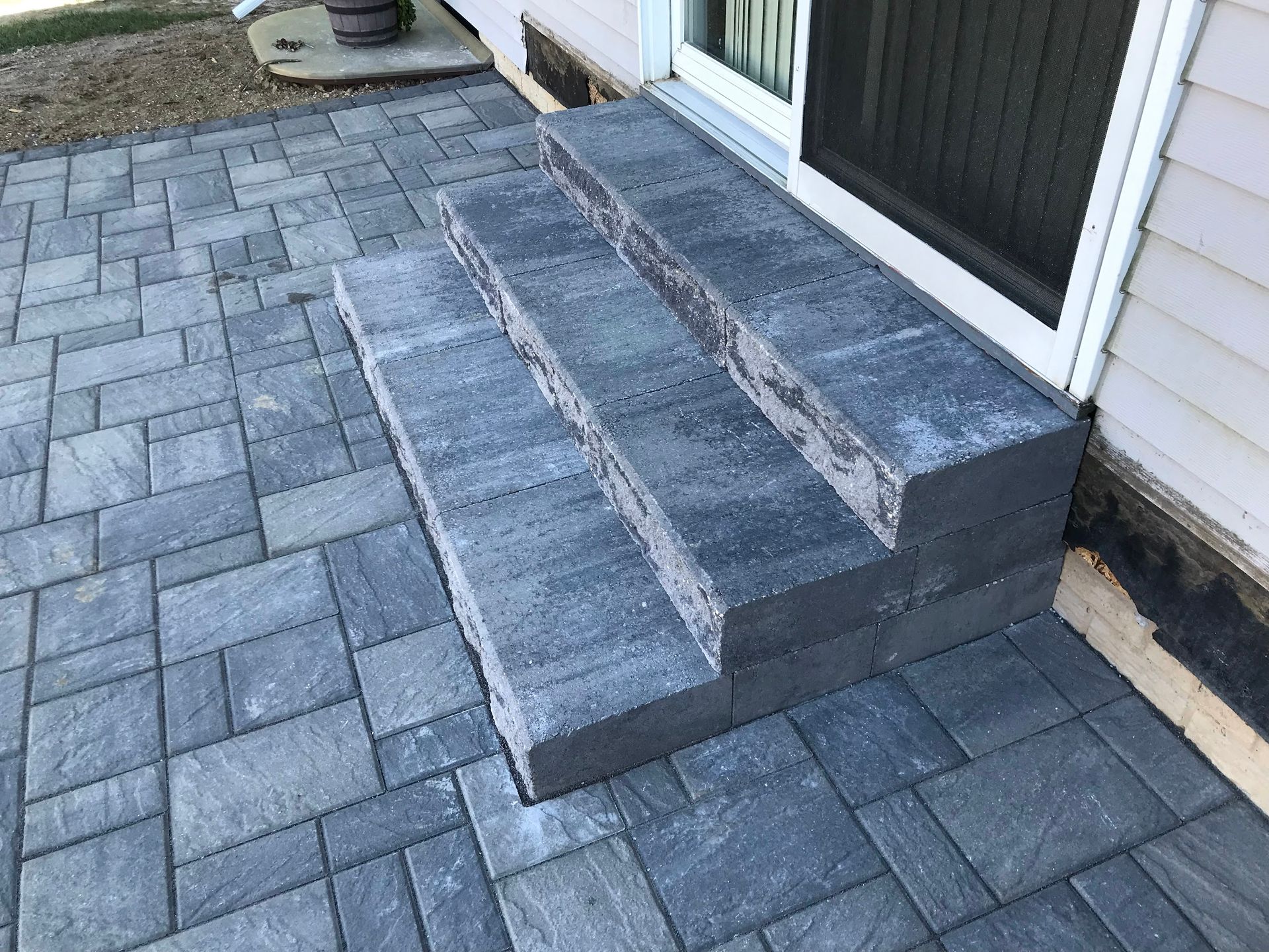Stone steps leading up to a sliding glass door. Dark gray pavers form the steps and patio.