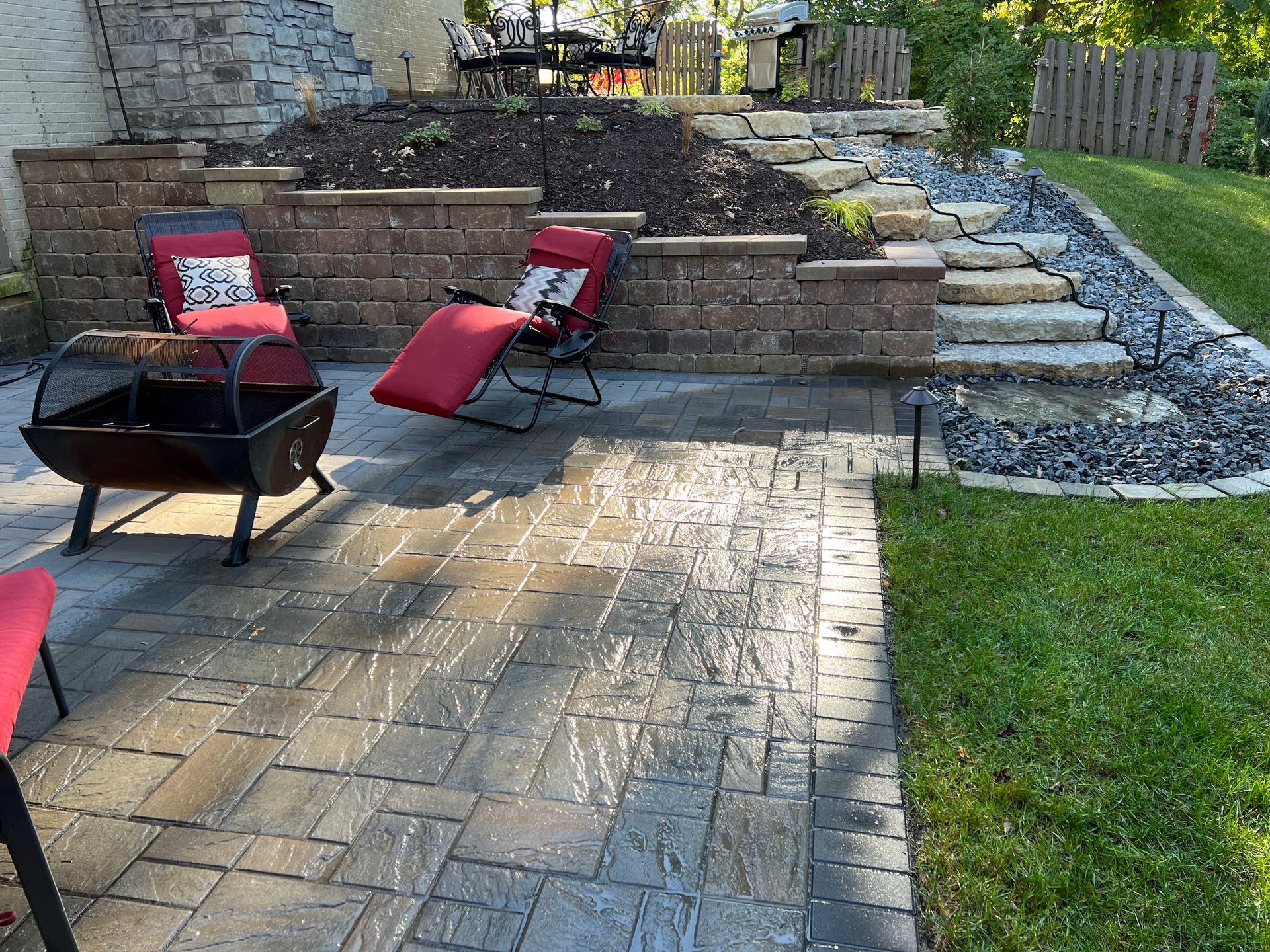 Brick patio with seating area, fire pit, and terraced landscaping with stairs and retaining walls.
