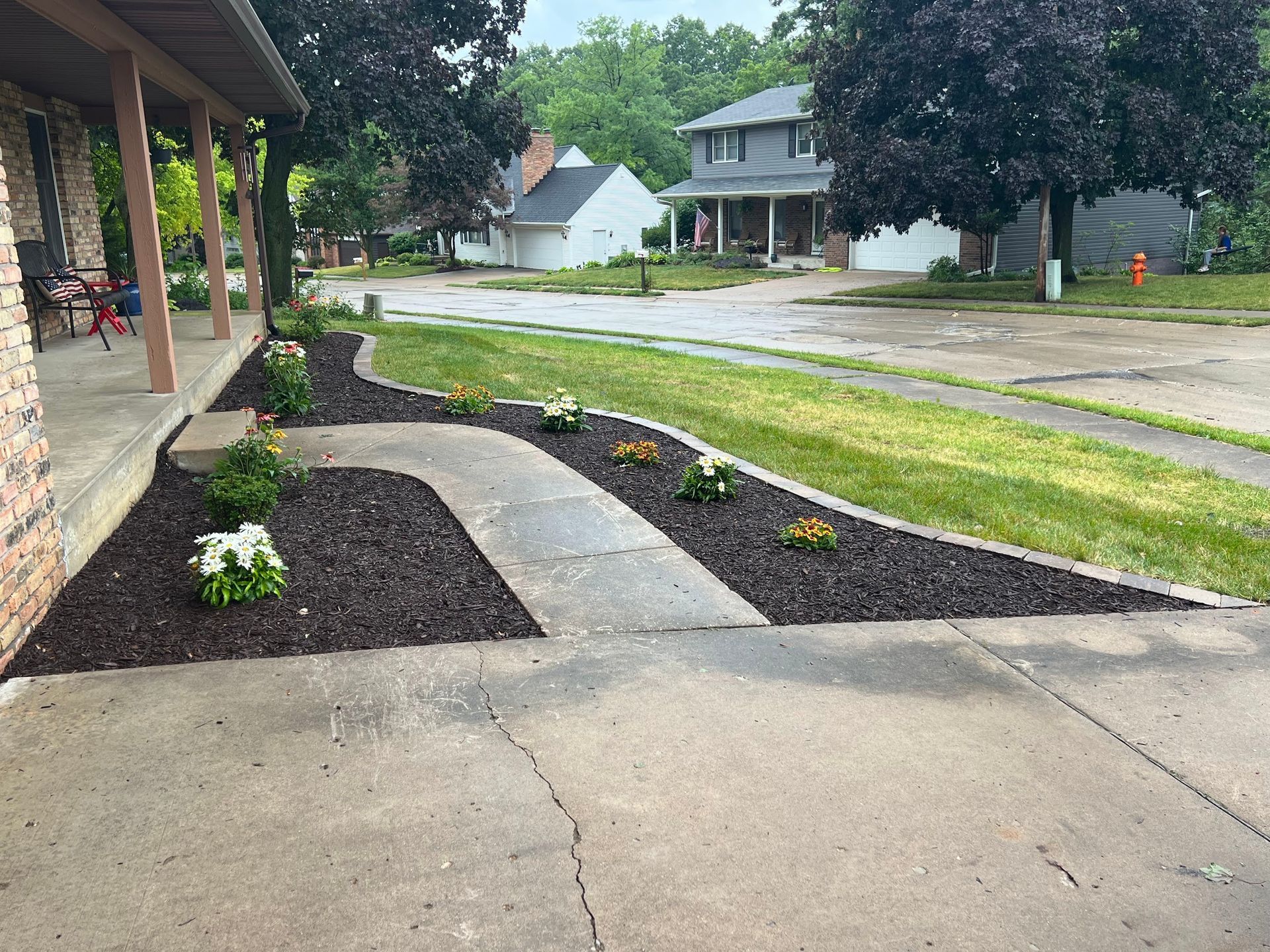A landscaped front yard with a brick home. Flowers line the curved walkway and driveway.