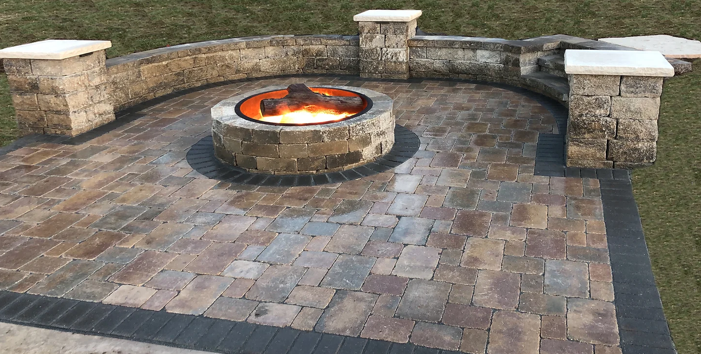 A stone patio with a lit fire pit, surrounded by a curved wall with seating.