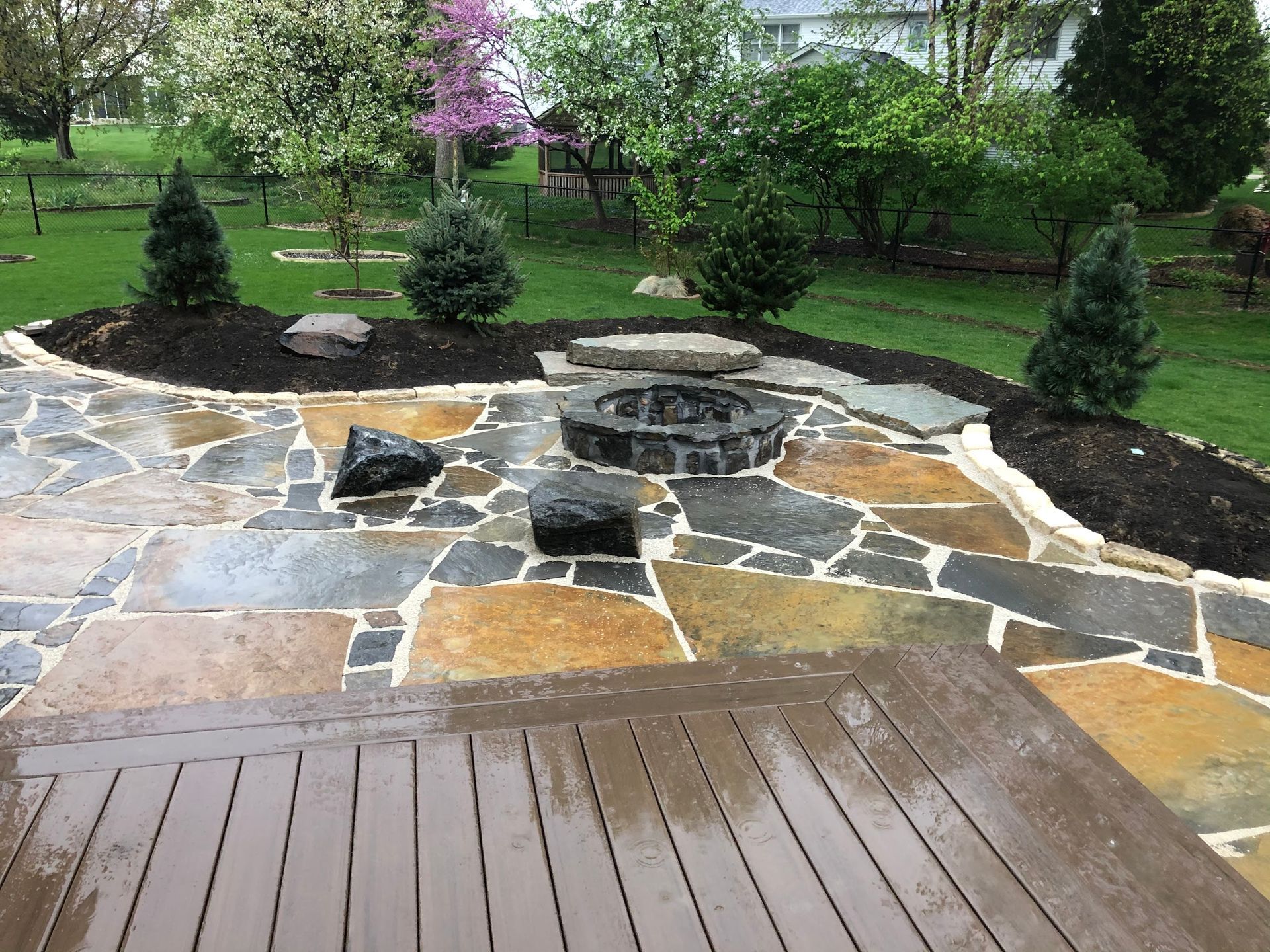 Patio with flagstone, fire pit, and landscaping on a cloudy day.